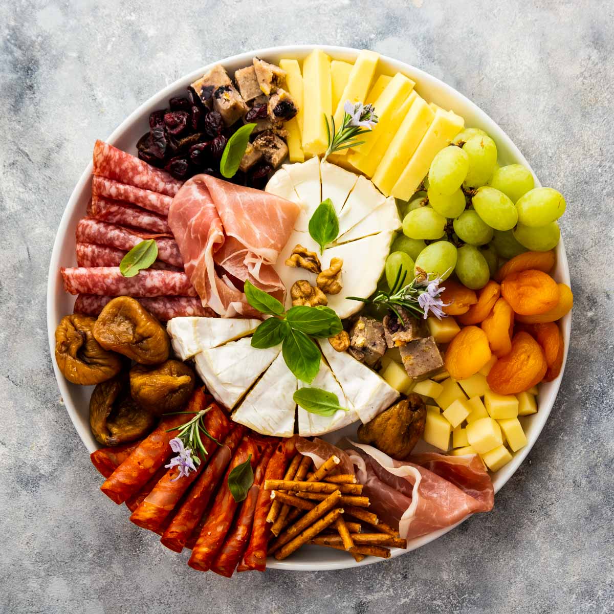 a closeup, overhead shot of a charcuterie board with brie, cubed cheeses, crostini, jam, grapes, dried apricots, and nuts