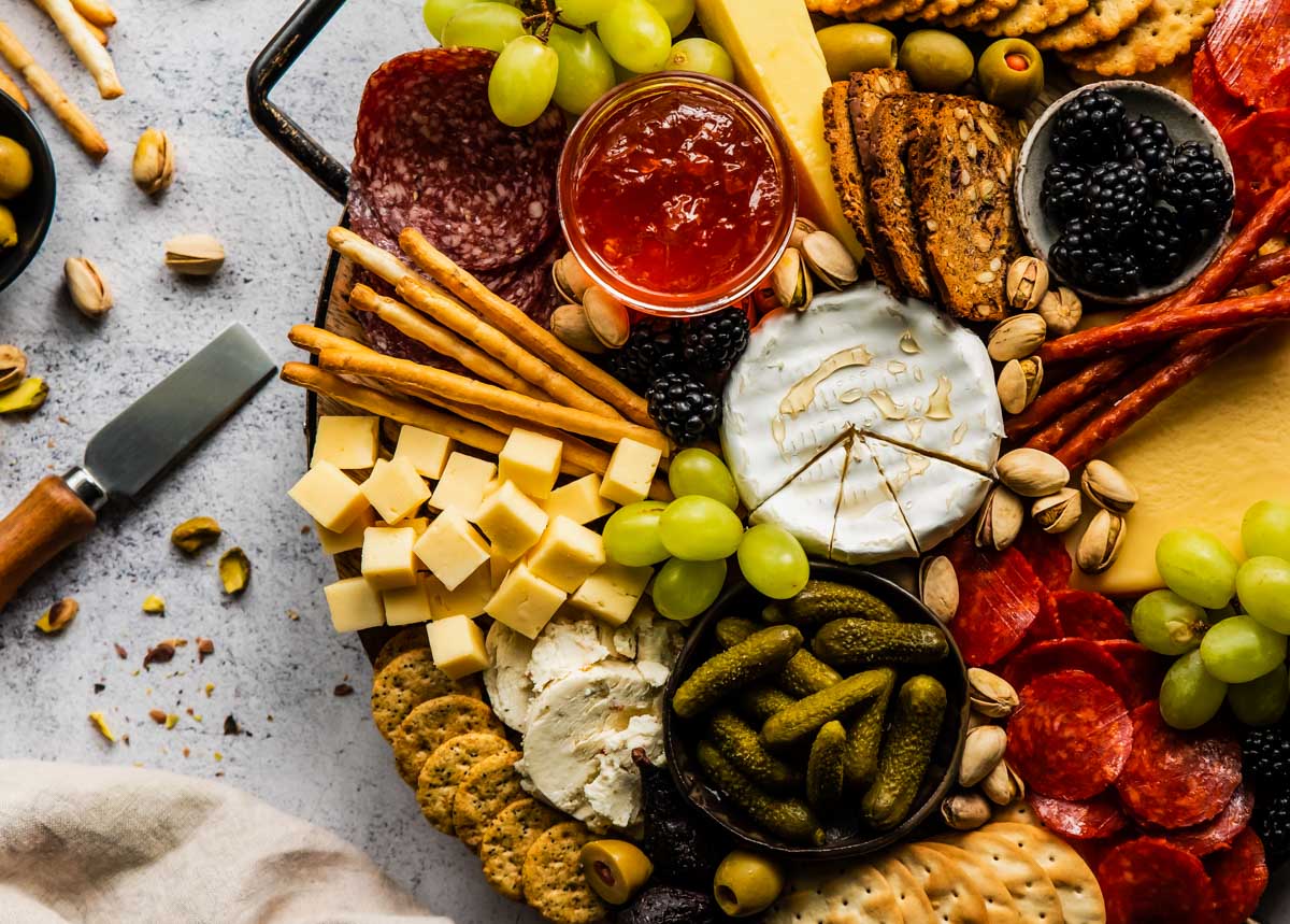 a closeup, overhead shot of a charcuterie board with brie, cubed cheeses, crostini, jam, grapes, and nuts