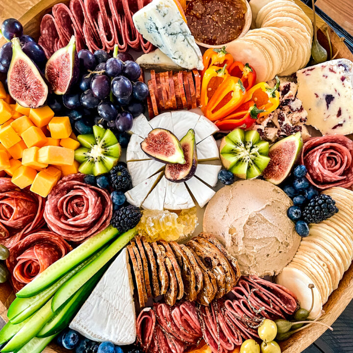 Large, round salami charcuterie board with brie, fresh vegetables, duck liver pâté, and crackers