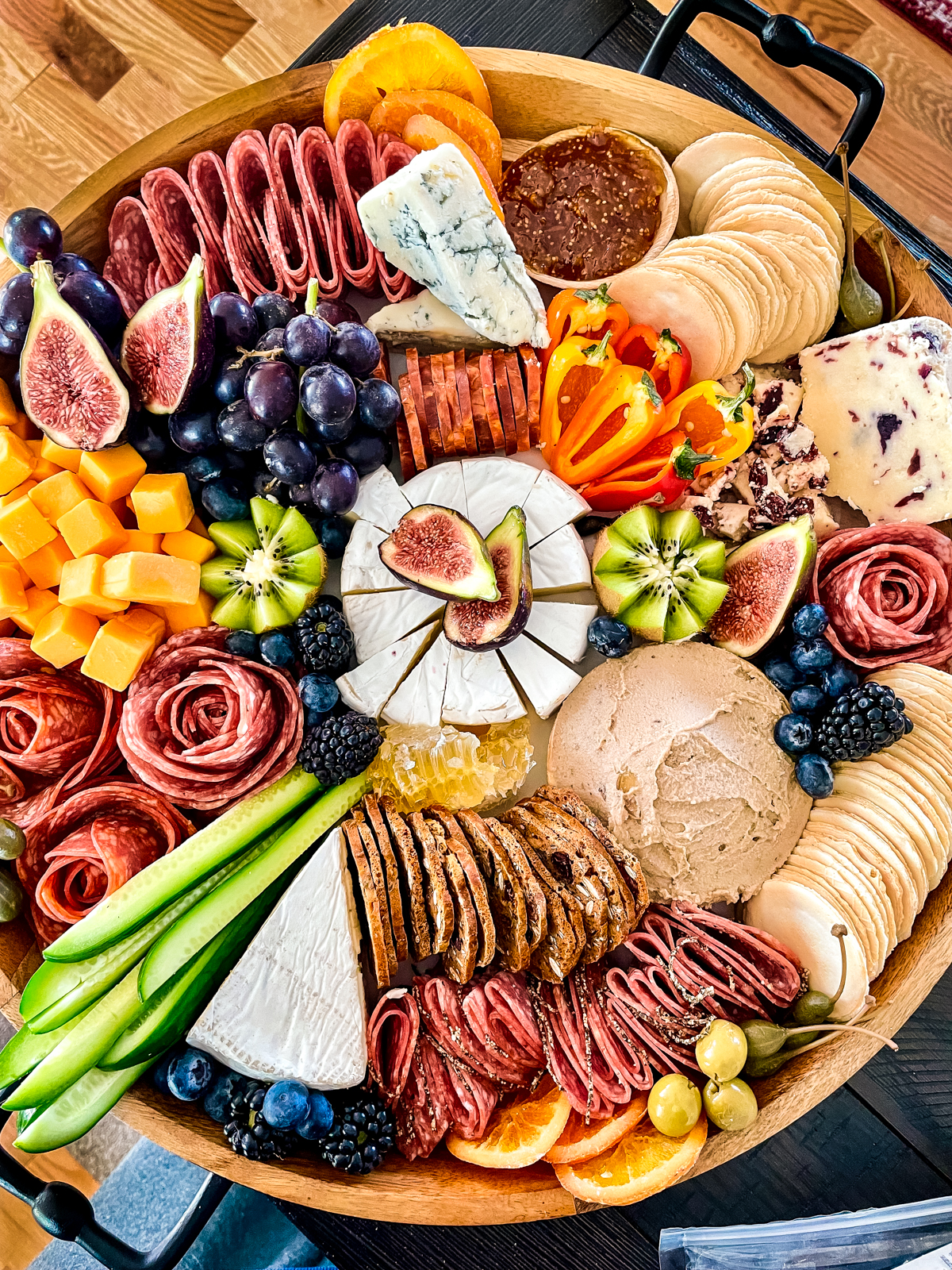 Large, round salami charcuterie board with brie, fresh vegetables, duck liver pâté, and crackers