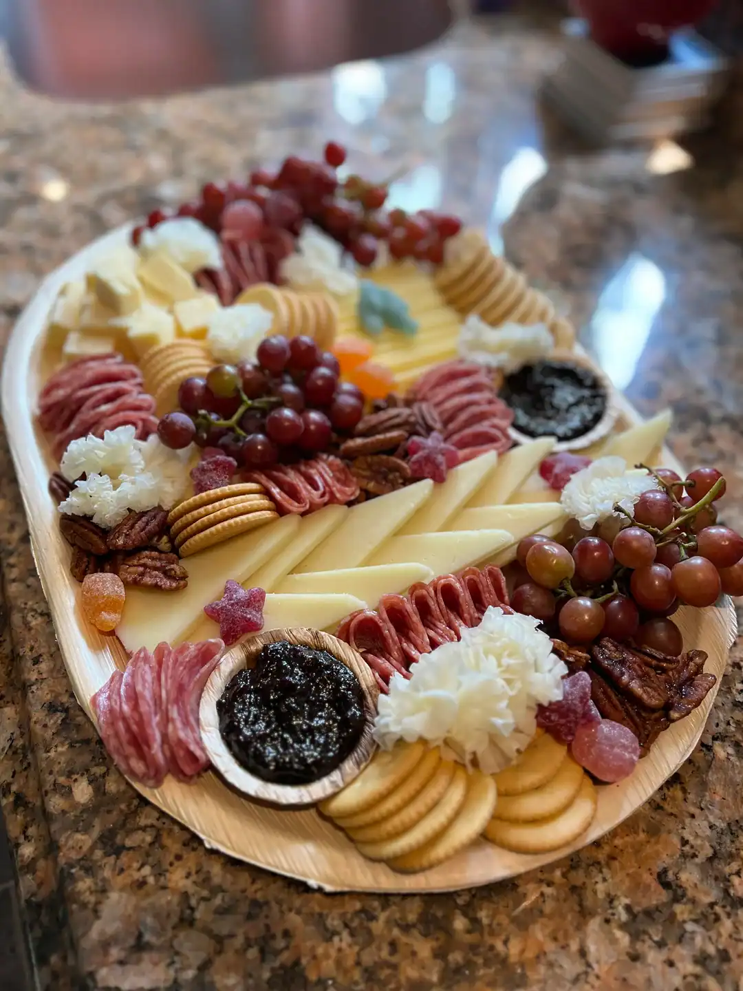a summer charcuterie board with Manchego, Wisconsin Cheddar, and Unexpected Cheddar, flowers made with Girolle, grapes, crackers, candied pecans, Calabrian Salami, Applewood smoke Salami, and Fig butter.