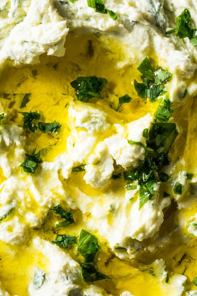 an extreme closeup shot of boursin dip topped with fresh herbs and olive oil