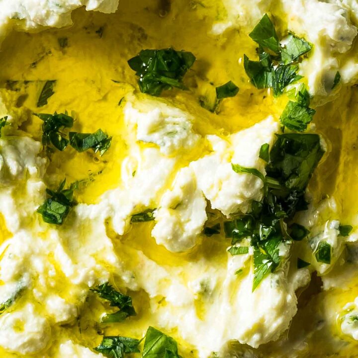 an extreme closeup shot of boursin dip topped with fresh herbs and olive oil
