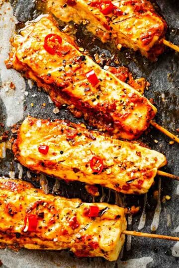 four skewers of hot honey halloumi cheese on parchment paper and garnished with thinly slice red chile peppers