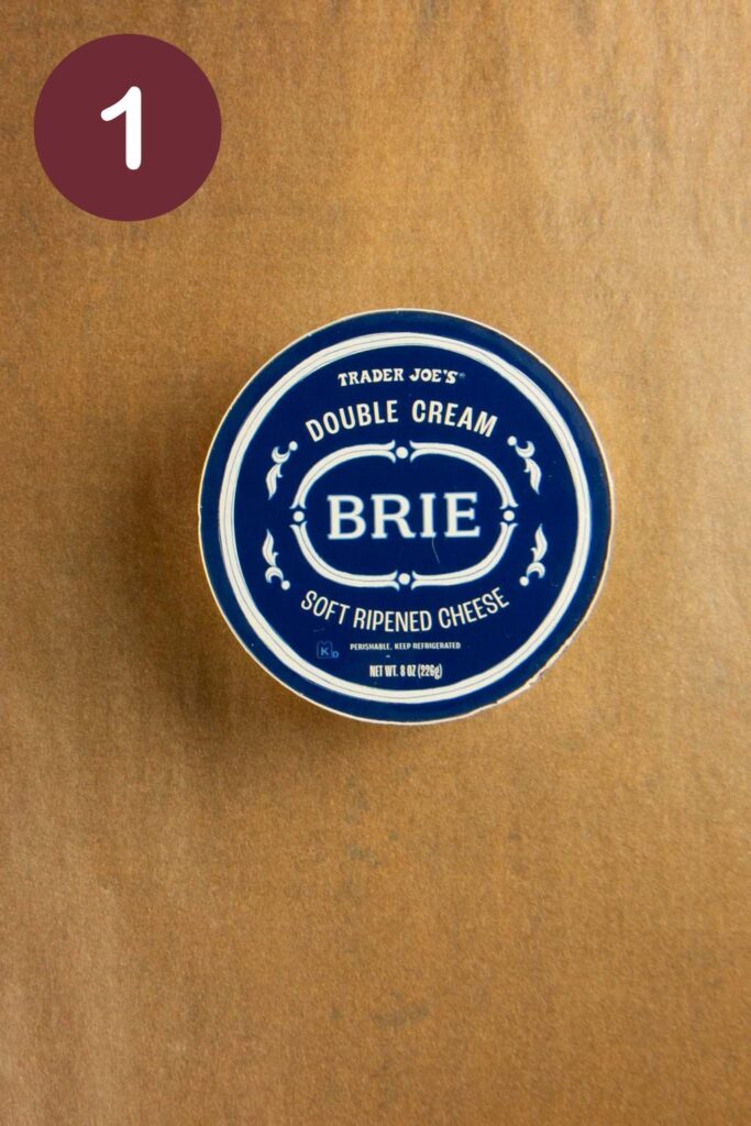 Step one of how to cut Trader Joe's Double Cream Brie: an unopened box on parchment paper with a round circle and a white #1