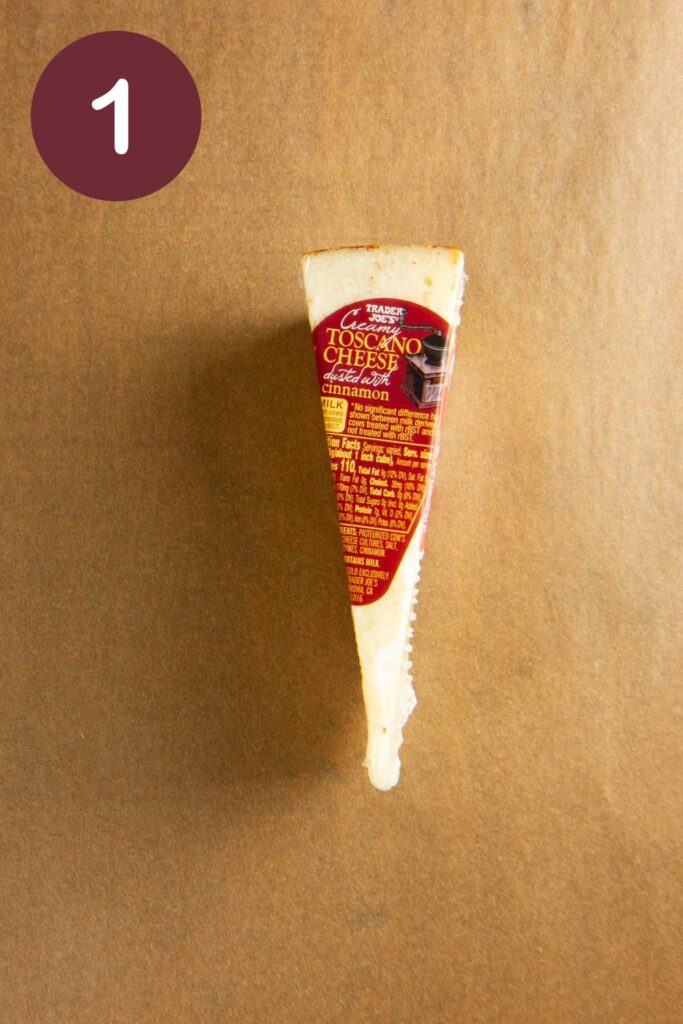 Step one of how to cut Trader Joe's Toscano cheese: an unopened package on parchment paper with a round circle and a white #1