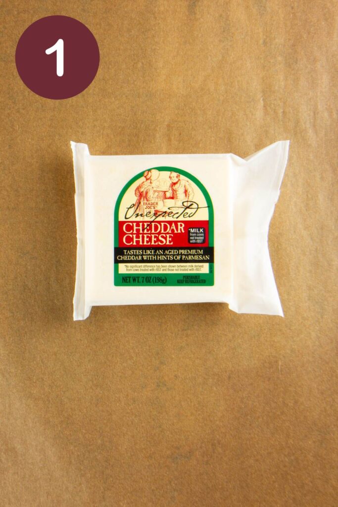 Step one of how to cut Trader Joe's Unexpected Cheddar: an unopened package on parchment paper with a round circle and a white #1