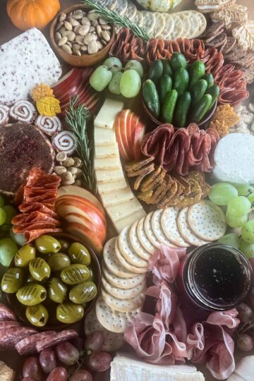 An overhead shot of a $100 Trader Joe's grazing table filled with cured meats, cheeses, and accoutrements with fall additions like maple leaf cookies, tiny leaf shortbread cookies, pumpkin biscotti and colorful gourds