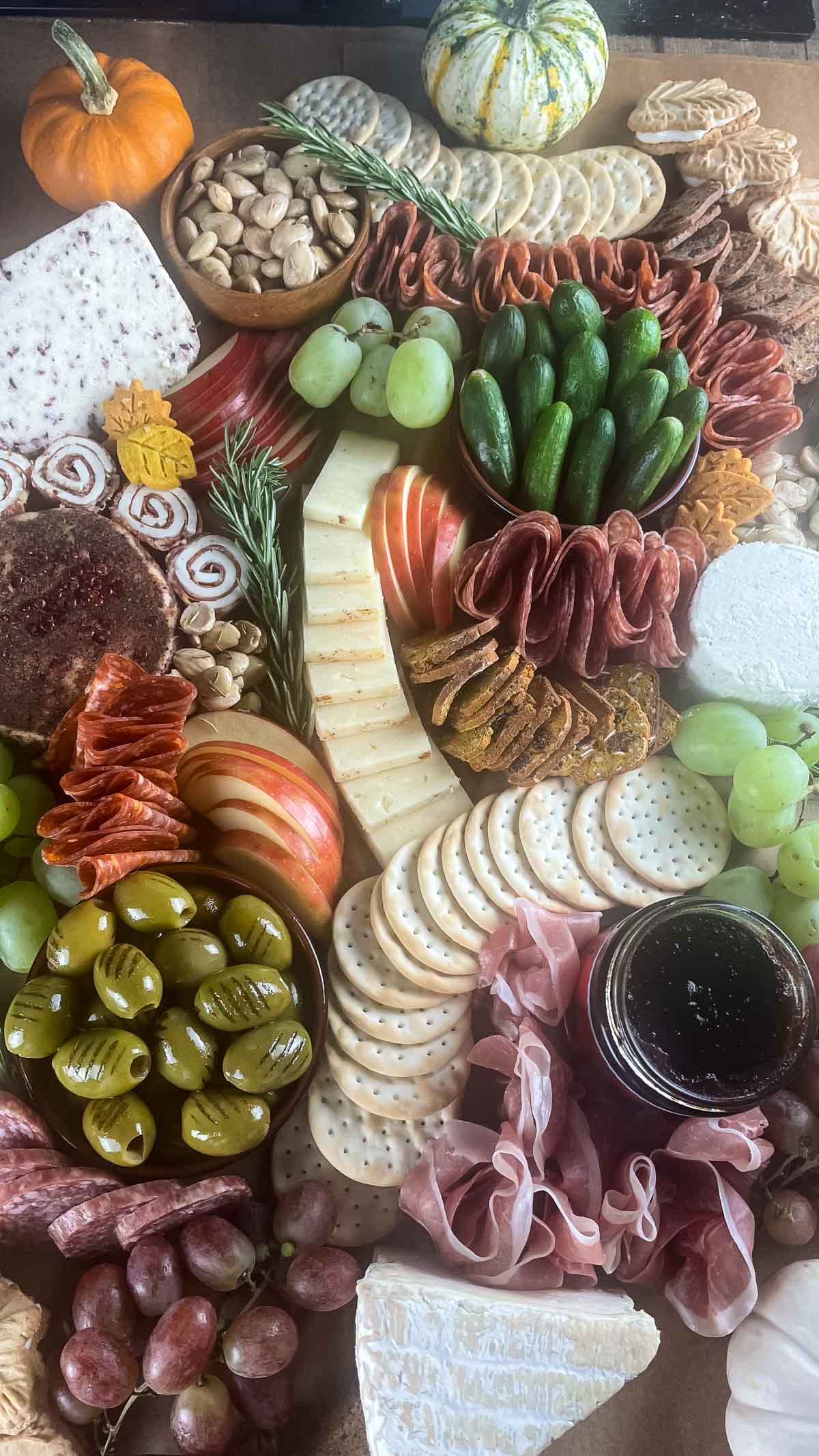 An overhead shot of a $100 Trader Joe's grazing table filled with cured meats, cheeses, and accoutrements with fall additions like maple leaf cookies, tiny leaf shortbread cookies, pumpkin biscotti and colorful gourds