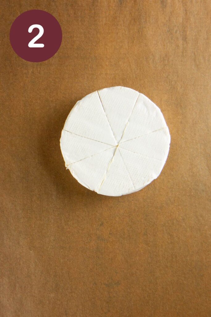 Step two of how to cut Trader Joe's Double Cream Brie: a wheel of the cheese on parchment paper sliced for 8 wedges, with a round circle and a white #2
