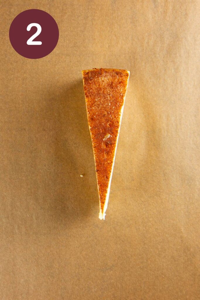 Step two of how to cut Trader Joe's Toscano cheese: an unwrapped, whole wedge on parchment paper with a round circle and a white #2