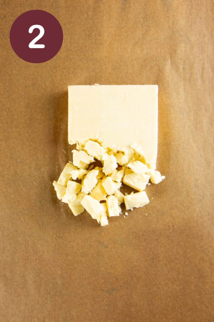 Step two of how to cut Trader Joe's Unexpected Cheddar: a block of the cheese on parchment paper with about ⅓ crumbled, with a round circle and a white #2