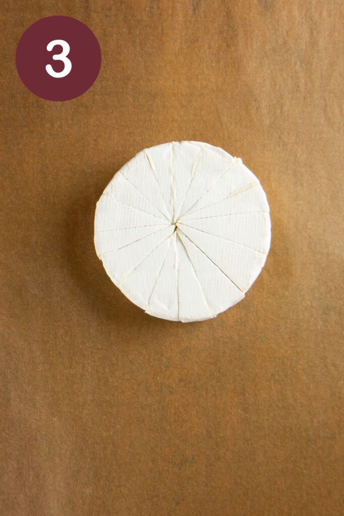 Step three of how to cut Trader Joe's Double Cream Brie: a wheel of the cheese with cuts to make 16 wedges on parchment paper with a round circle and a white #3