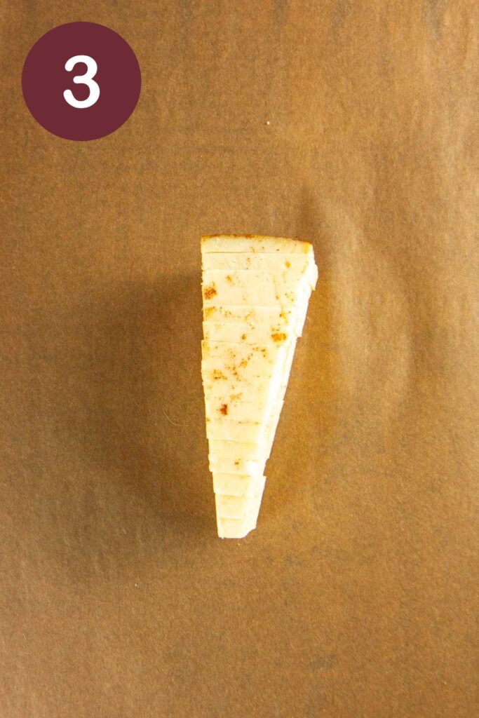 Step three of how to cut Trader Joe's Toscano cheese: a wedge that's been sliced into pieces on parchment paper with a round circle and a white #3
