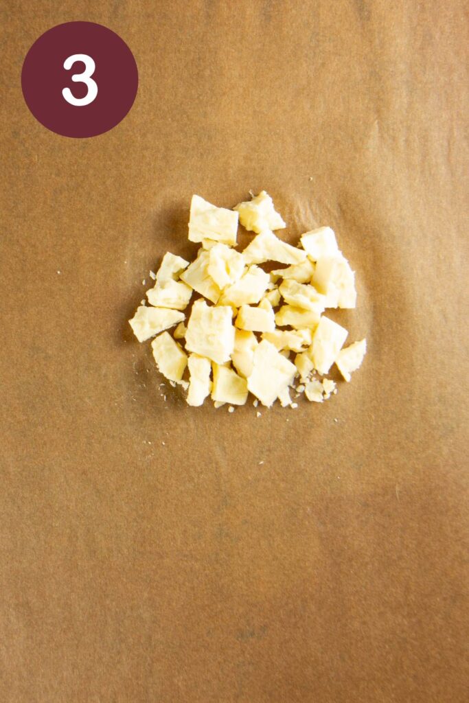 Step three of how to cut Trader Joe's Unexpected Cheddar: a small pile of the cheese crumbled on parchment paper with a round circle and a white #3