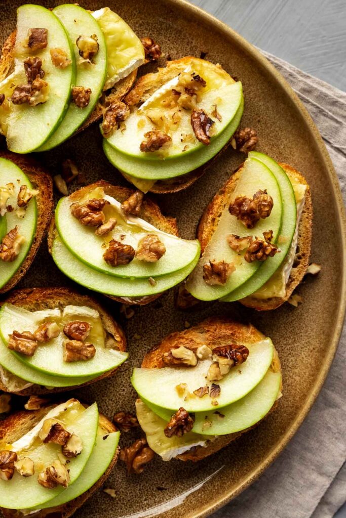 a large brown plate filled with apple and brie crostini with walnuts and drizzled honey