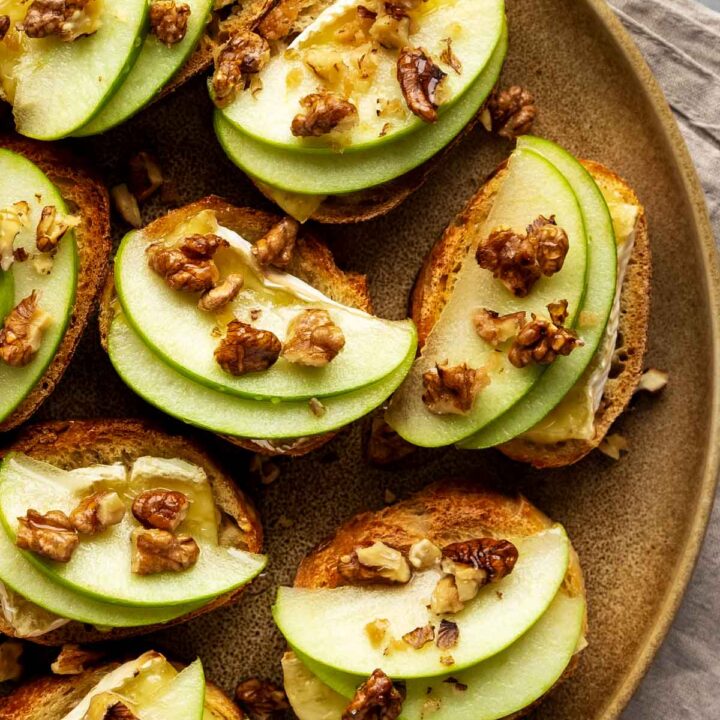 a large brown plate filled with apple and brie crostini with walnuts and drizzled honey
