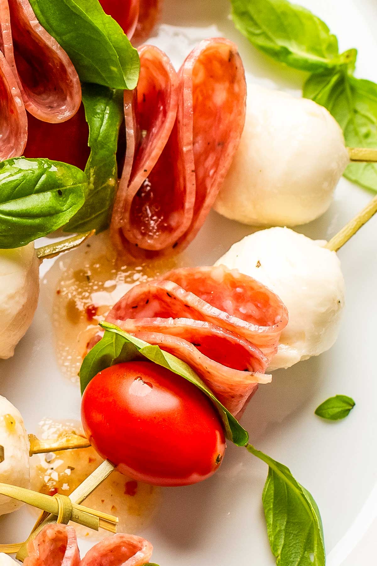 a closeup of a charcuterie skewer made with mozzarella, grape tomatoes, salami, and fresh basil