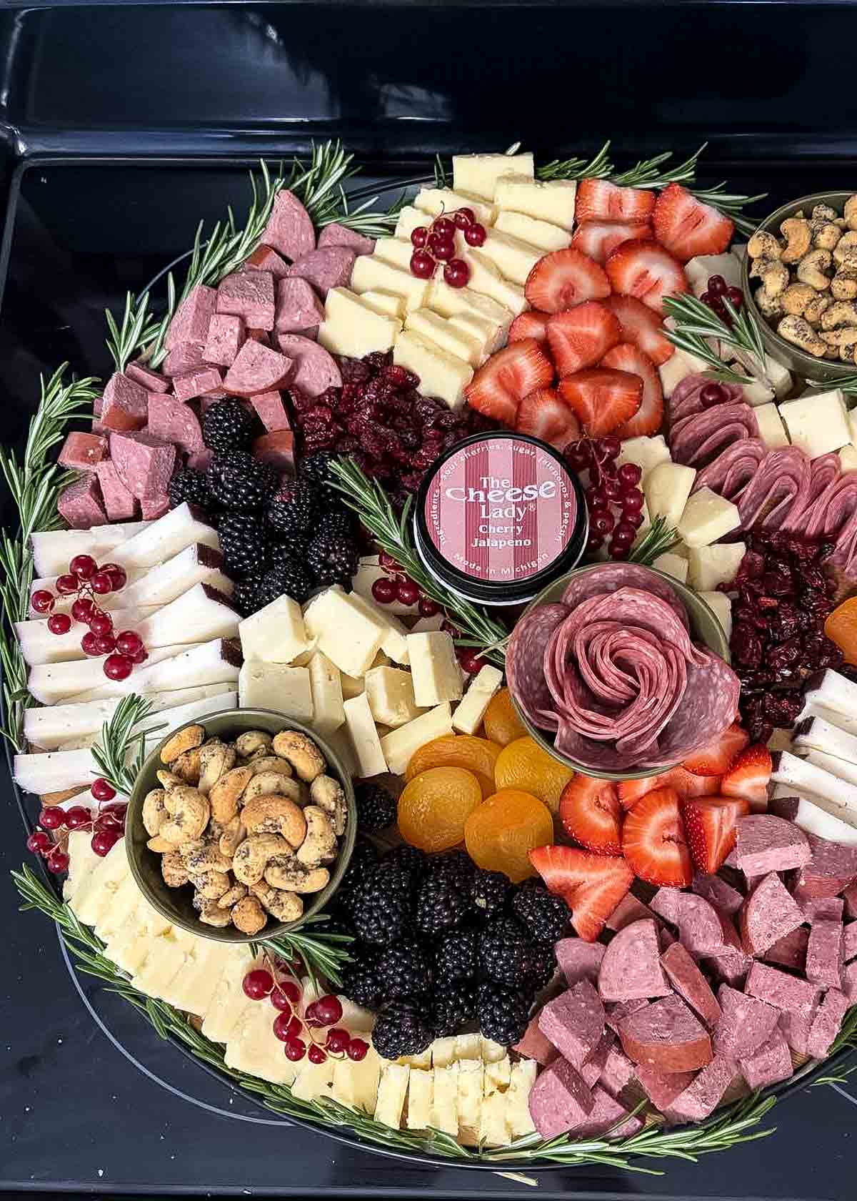 a large round christmas charcuterie board with cured meats, cheeses, a salami rose, fresh rosemary, nuts, strawberries, and pomegranate arils